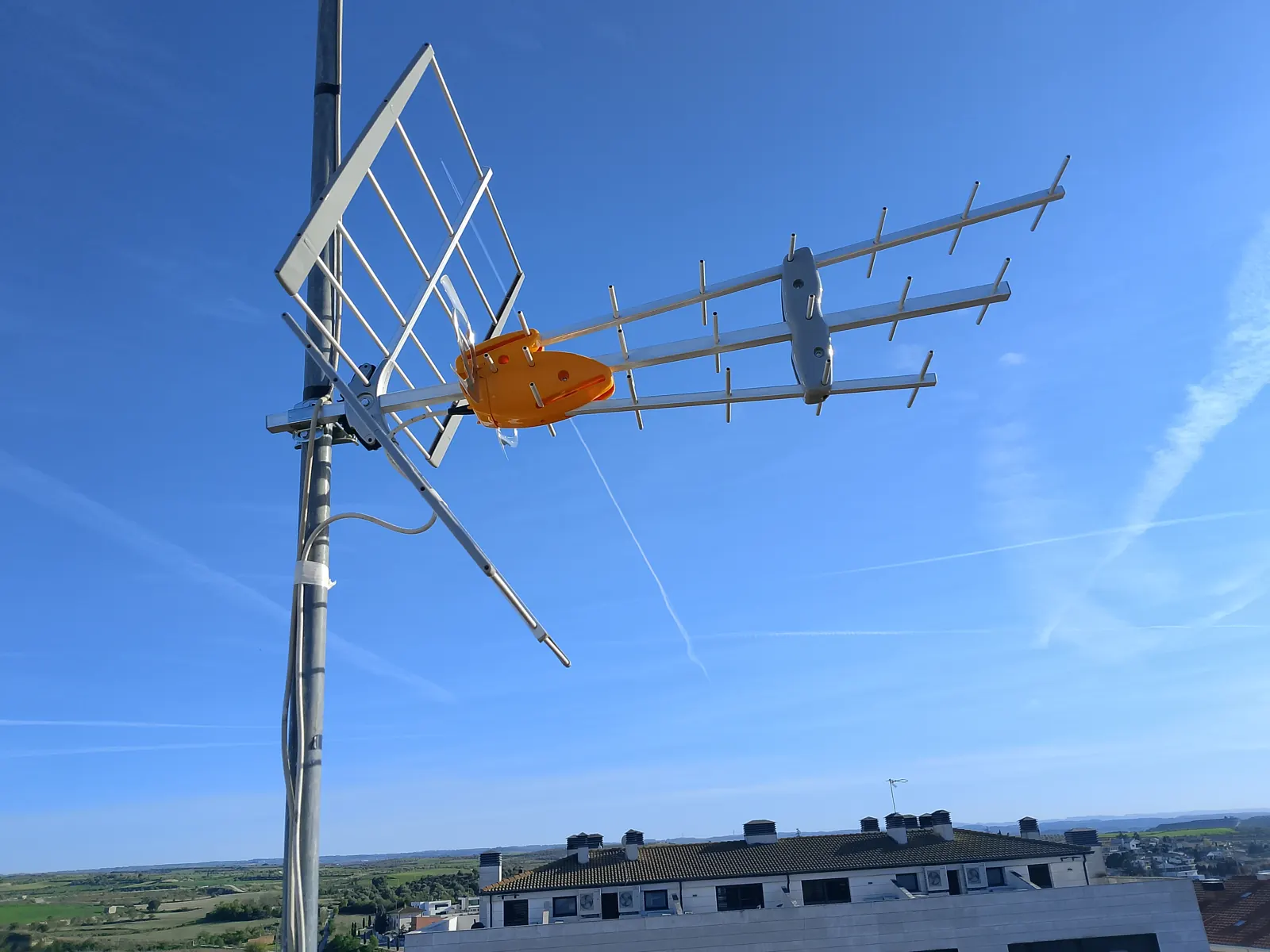 Antena de TDT i parabòlica en màstil sobre teulada.